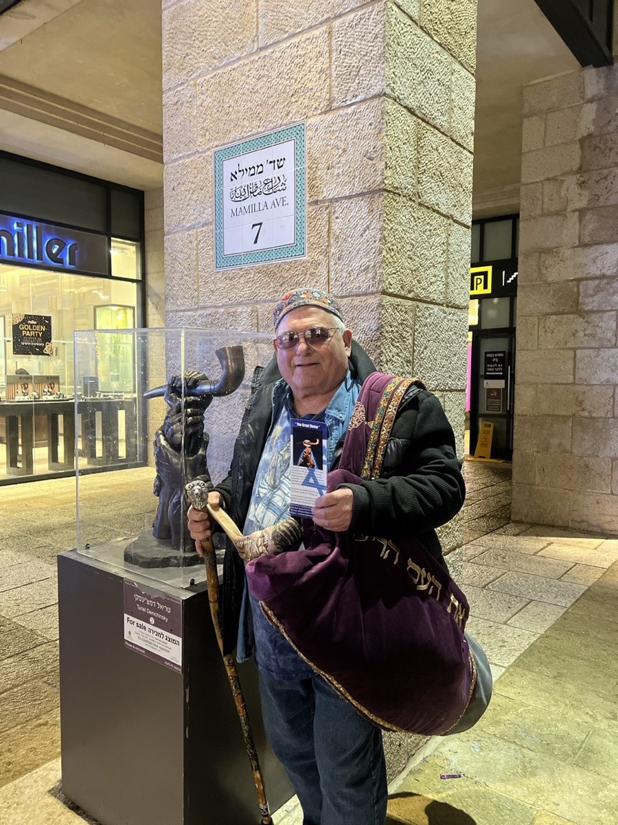 Robert Weinger standing beside The Great Shofar sculpture at Mamilla Avenue 7, Jerusalem, holding a shofar and exhibition flyer