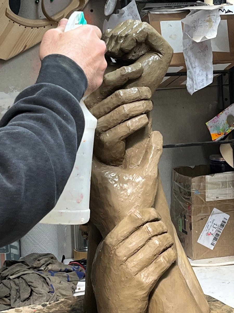 The sculptor's hands working the clay, shaping the intertwined grip
